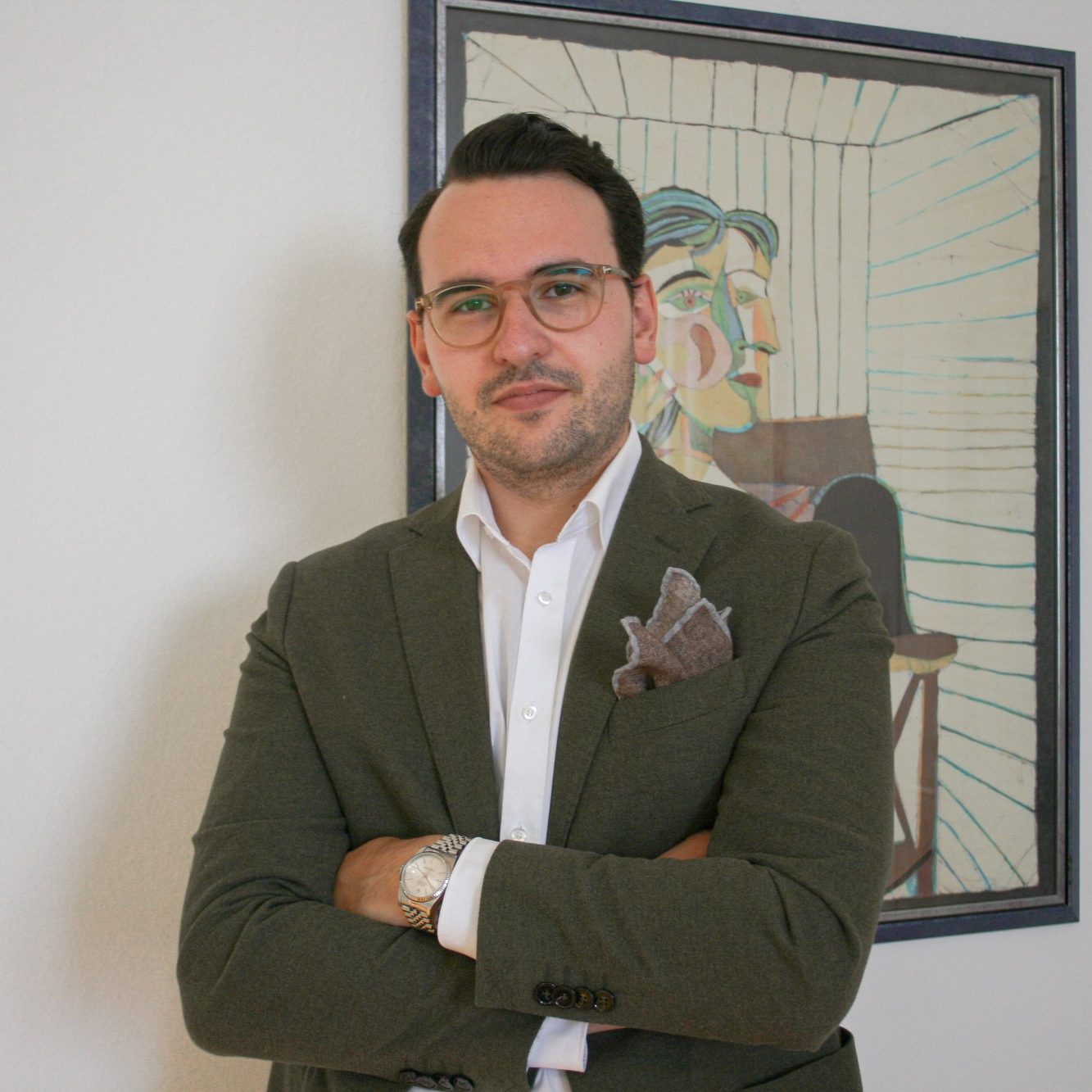 Mann mit Brille, trägt einen grünen Blazer, steht vor einem Kunstwerk.